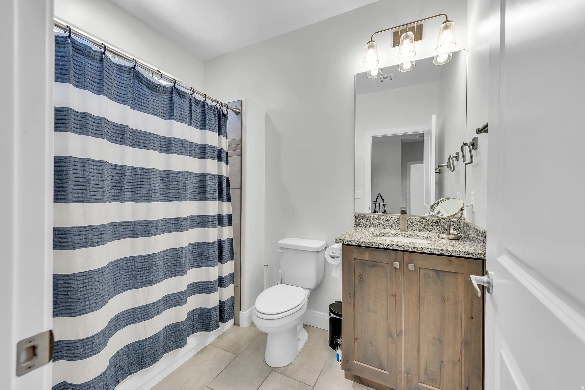 Bathroom featuring a wood-finish vanity with a stone countertop, an undermount sink, and a framed mirror