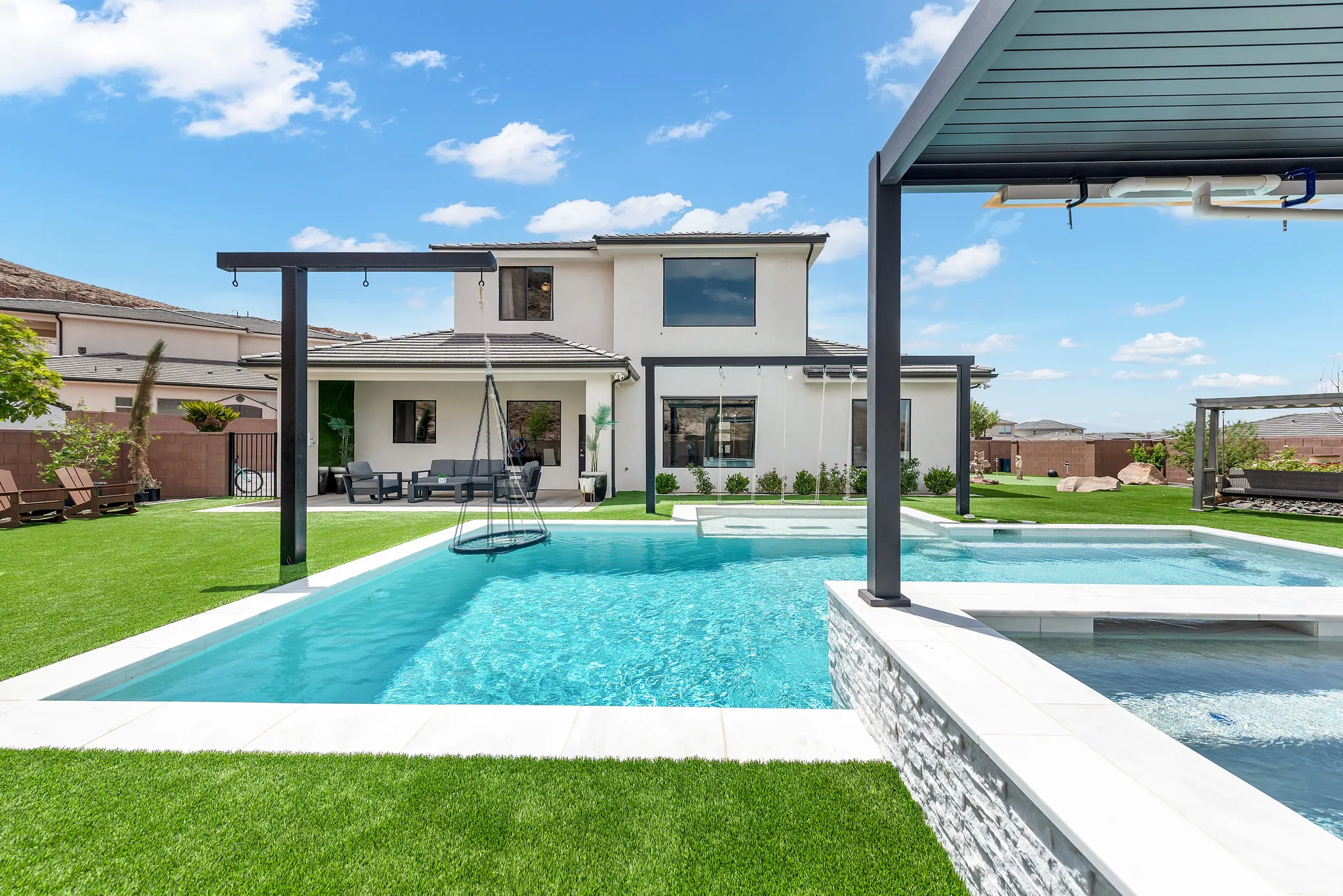 Contemporary two-story residence featuring a large rectangular pool, integrated spa, and expansive artificial turf