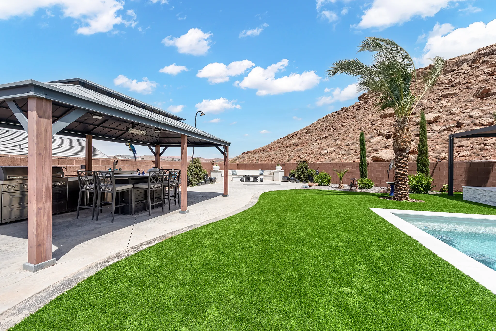 Outdoor entertainment area featuring a covered patio with an integrated kitchen and seating, a manicured lawn, and a swimming pool