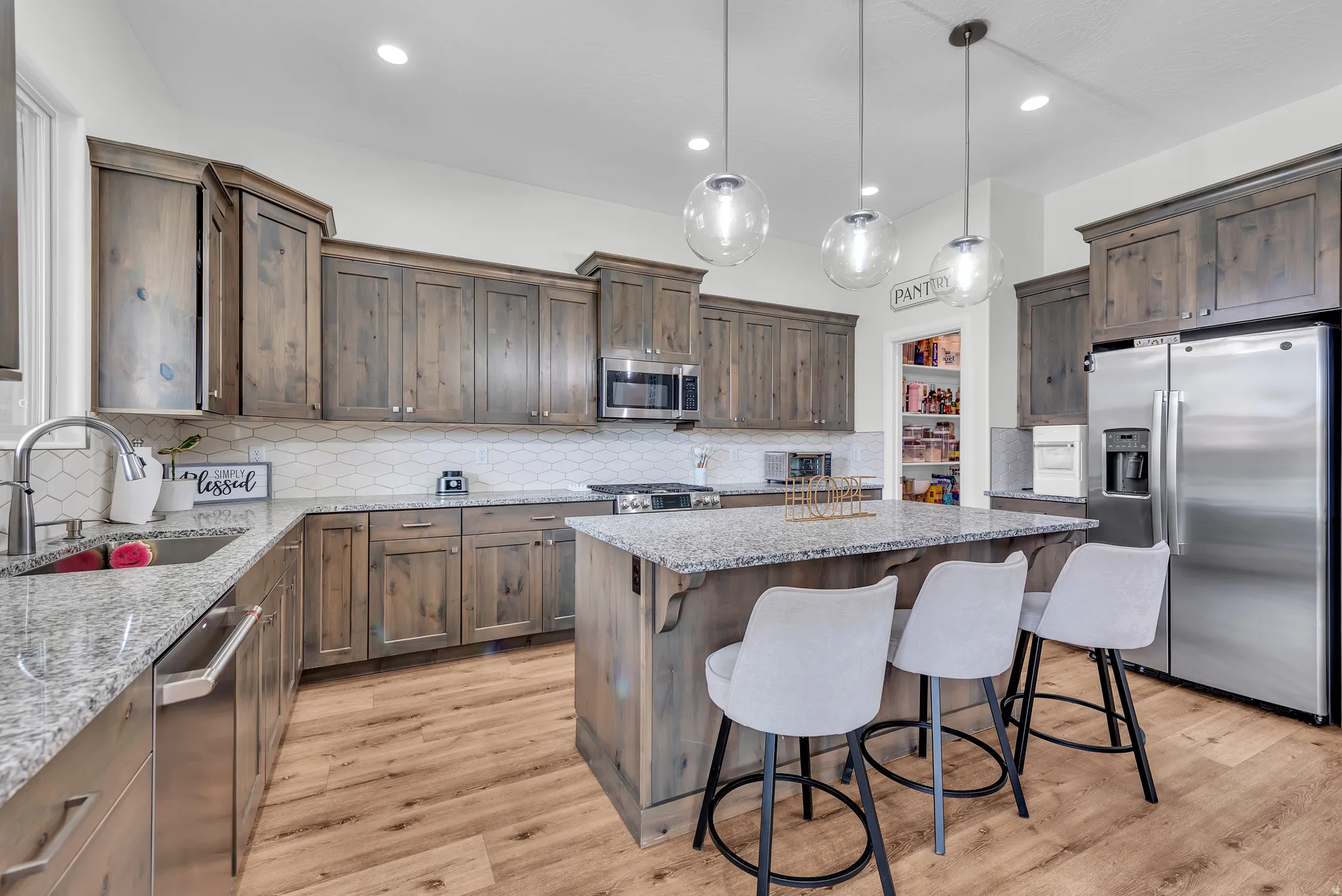 Spacious kitchen featuring an island with pendant lighting, wood-finish flooring, stainless steel appliances, and ample cabinetry