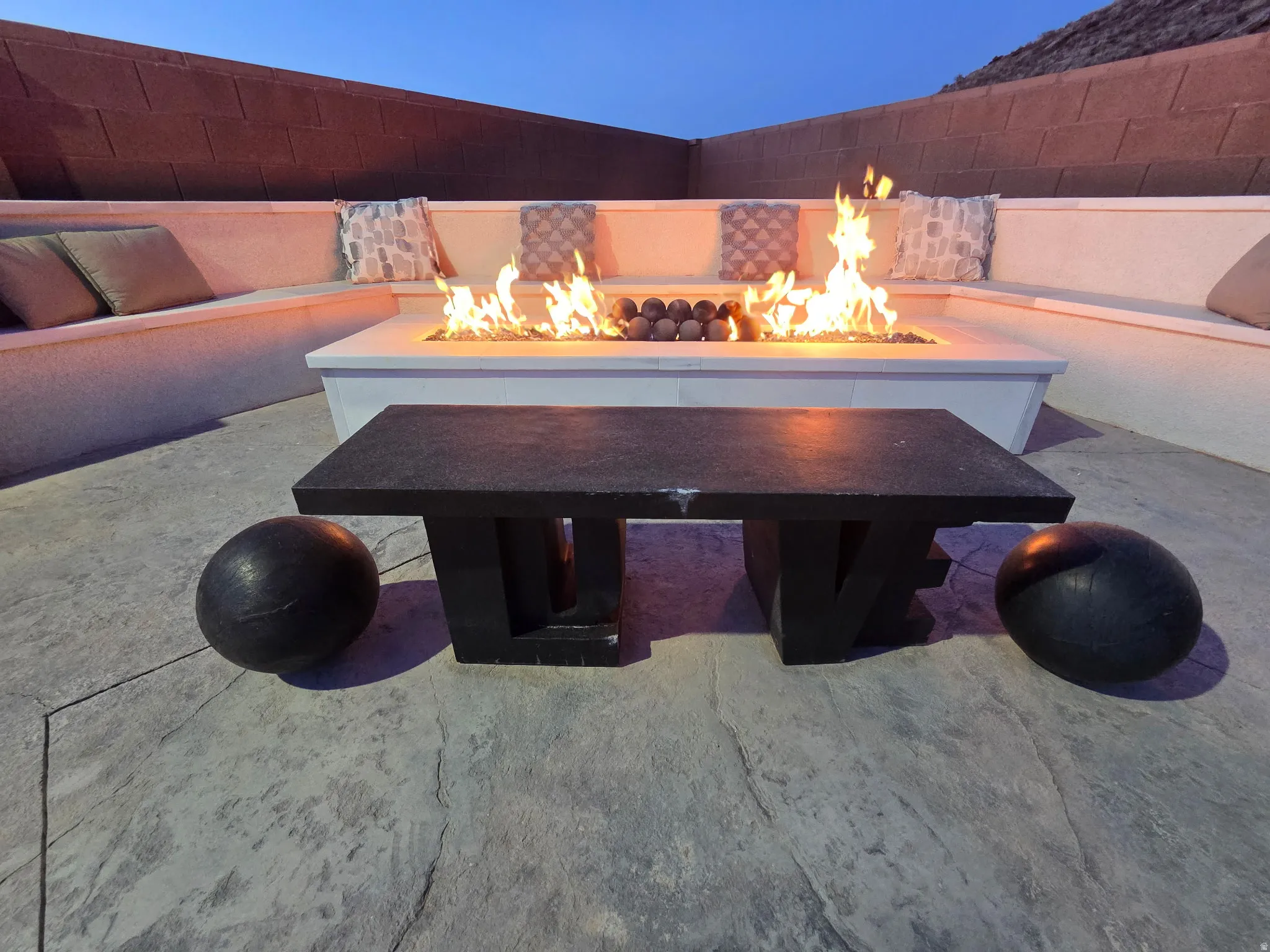 Outdoor living area featuring a built-in fire pit, integrated bench seating, and patterned concrete flooring