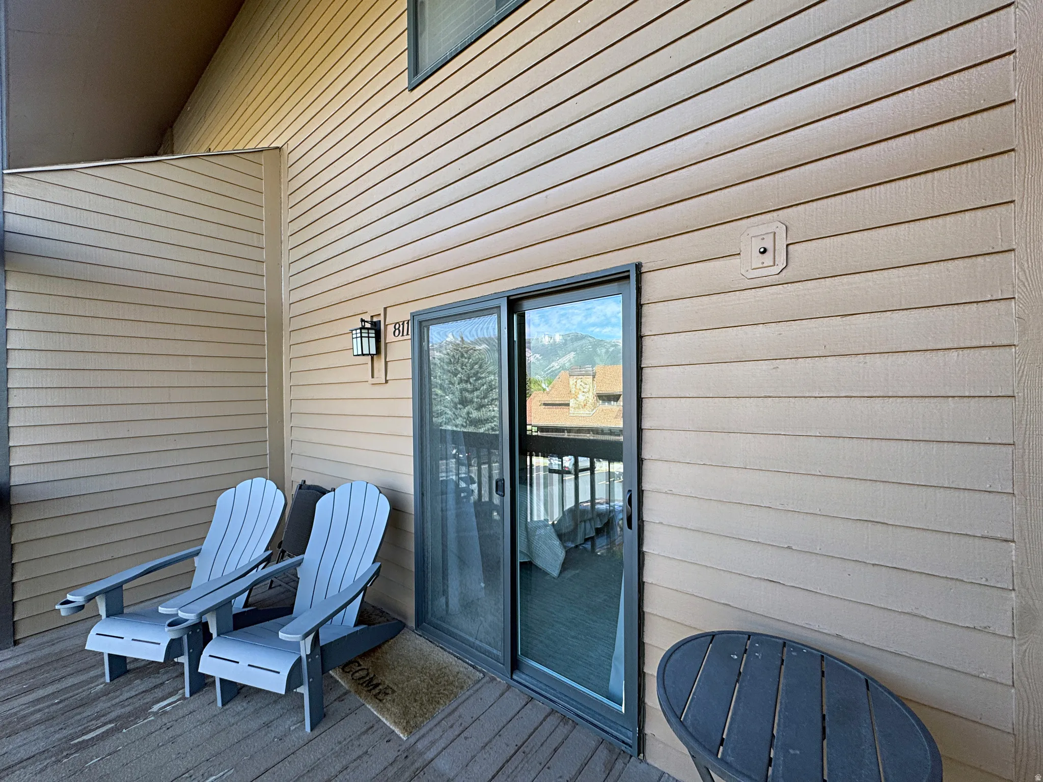 Spacious balcony with wood-finish flooring, featuring horizontal siding, dark-framed sliding glass doors, and an exterior wall lantern