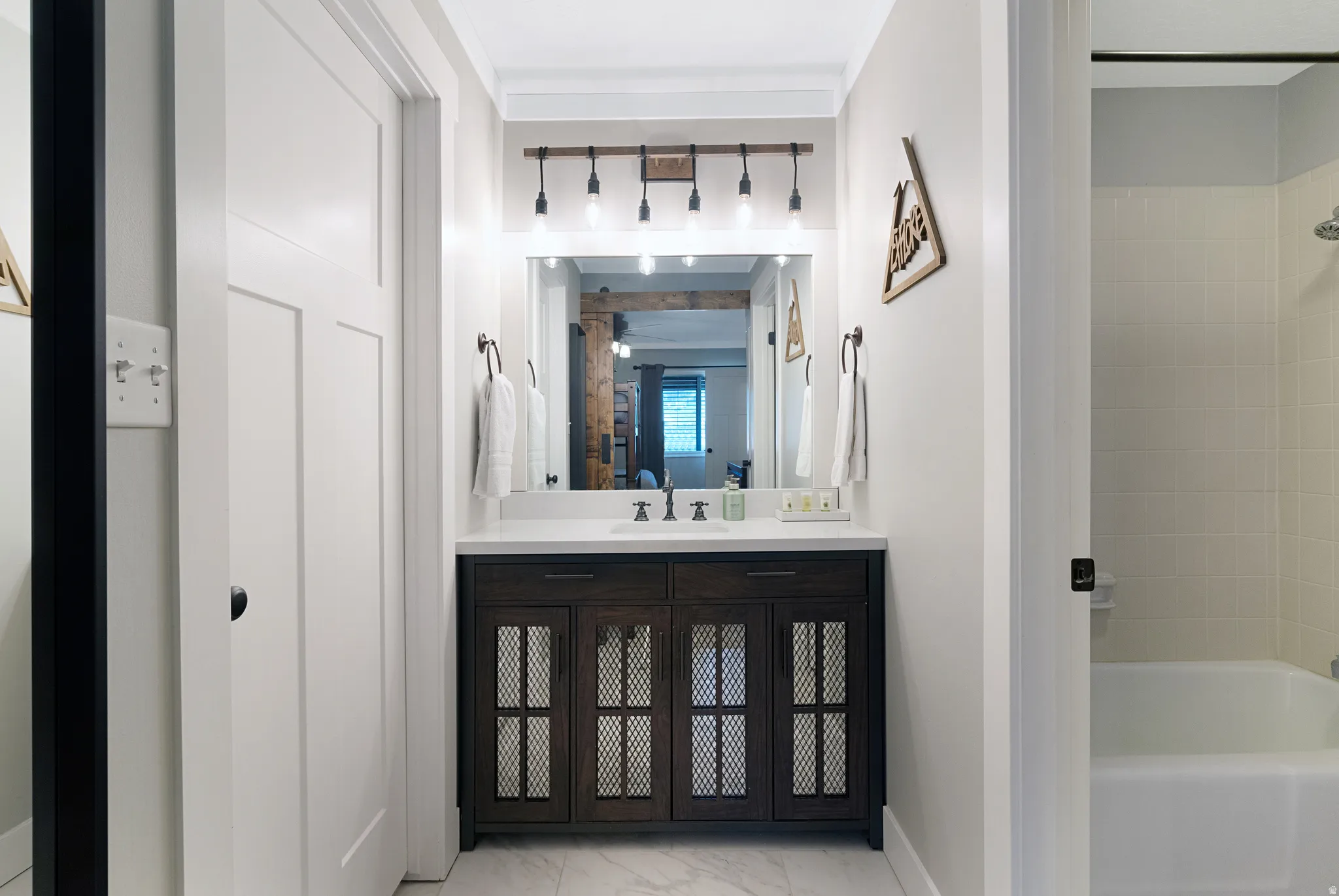 Modern bathroom featuring a dark wood-finish vanity with mesh inserts, a white countertop, and a large mirror