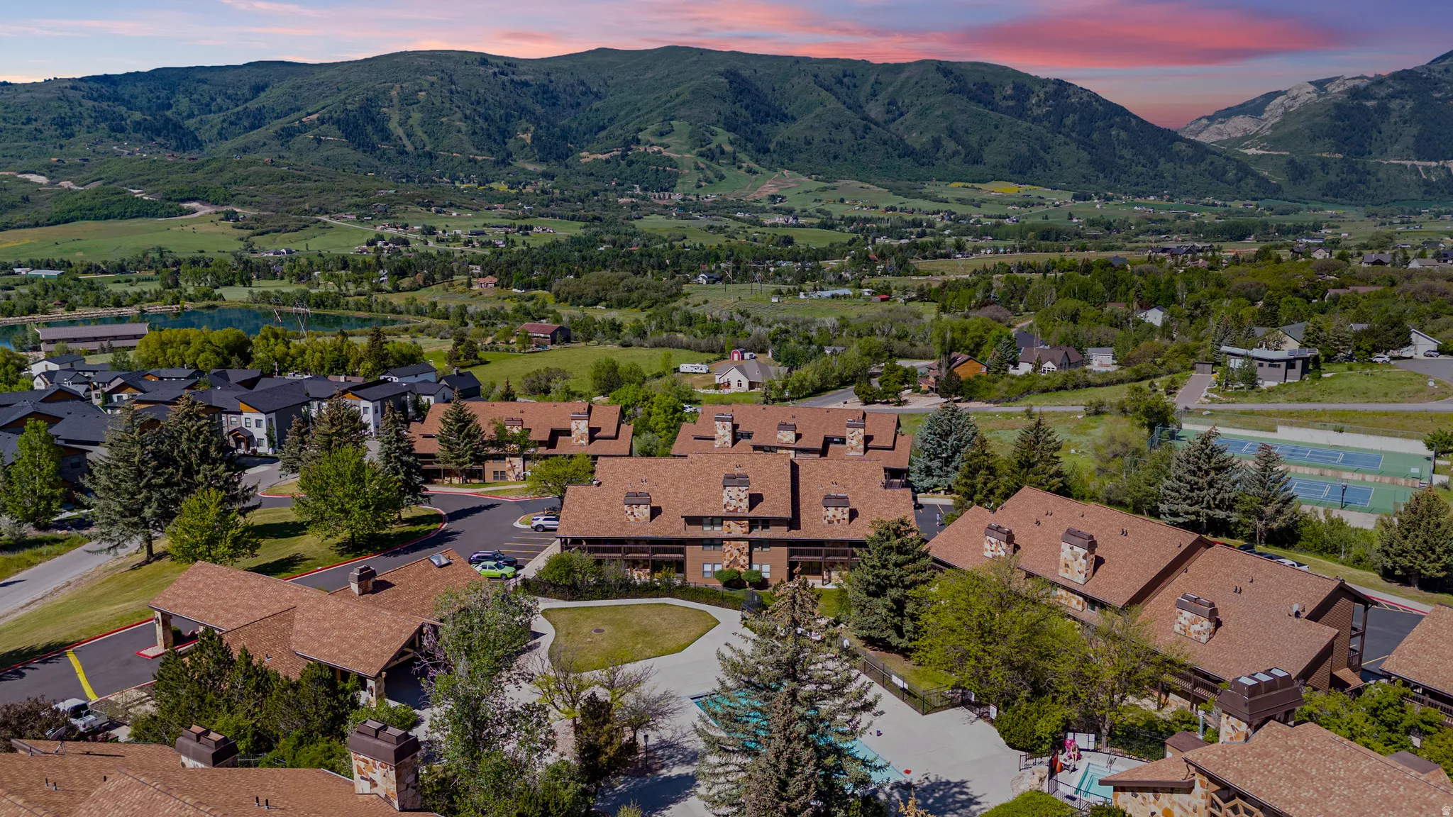Aerial perspective showcasing a complex of buildings with brown shingle roofs and stone accents, surrounded by mature trees