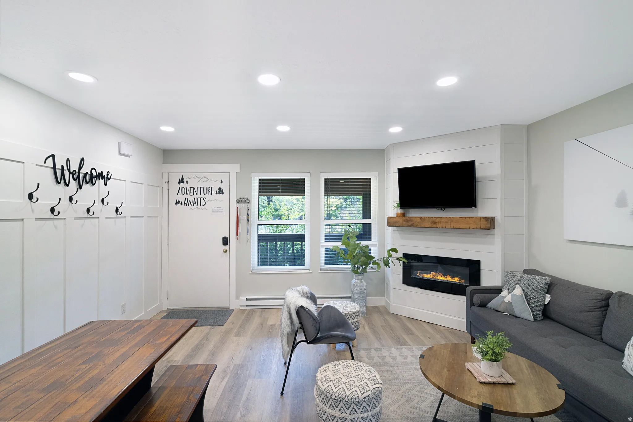 Open-concept living area with wood-finish flooring, recessed lighting, and a corner electric fireplace with a wood mantel
