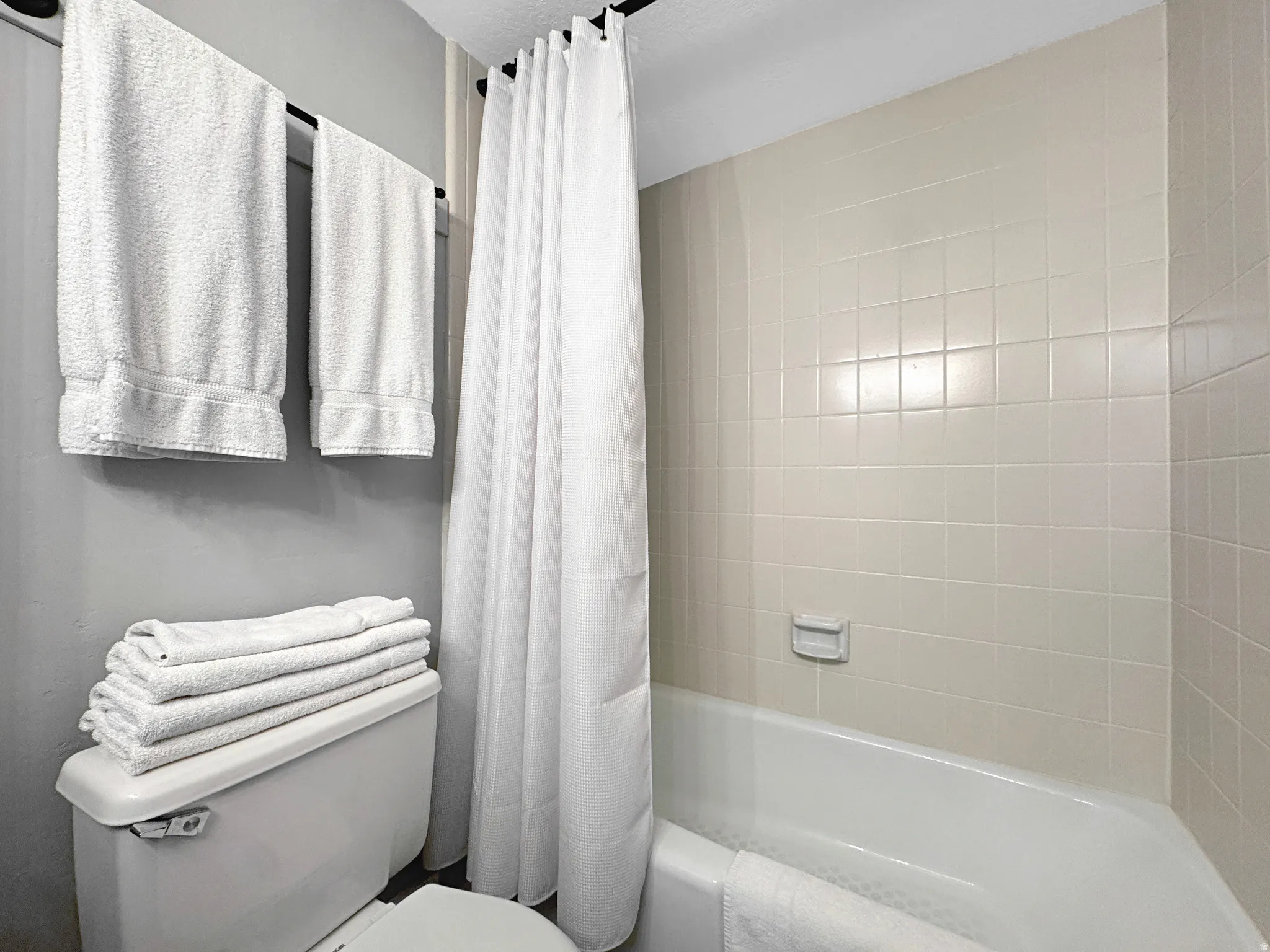 Bathroom featuring a white porcelain toilet, a white bathtub, and light-colored square wall tiles