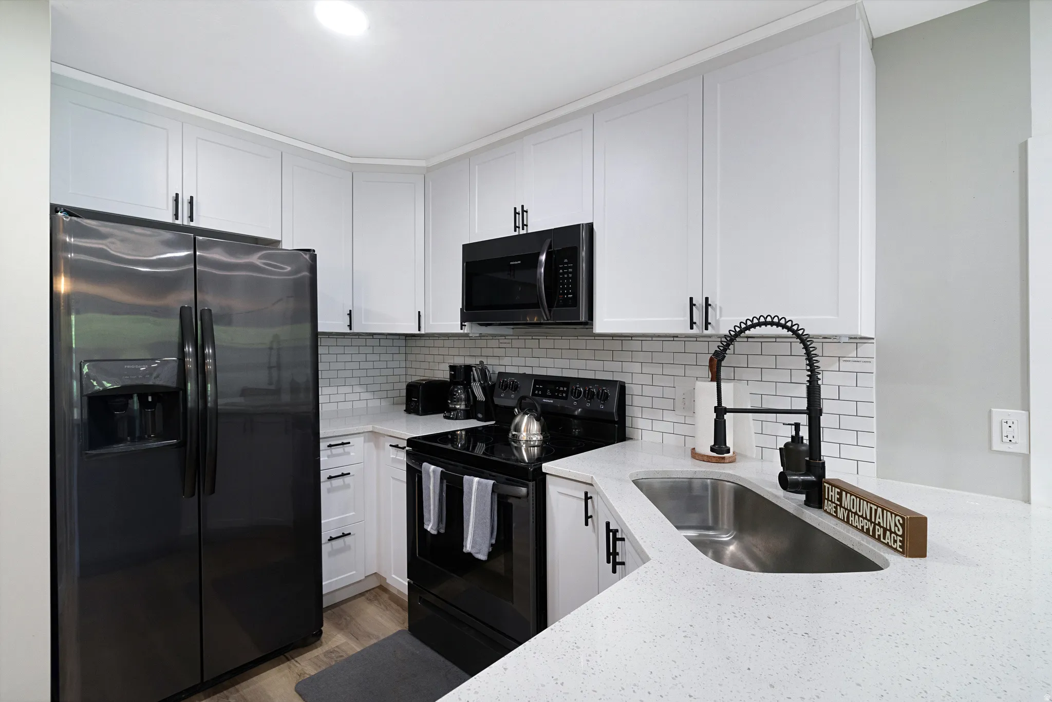 Contemporary kitchen featuring white shaker cabinetry, light-toned countertops, a subway tile backsplash, and a stainless steel sink with a matte black pull-down faucet