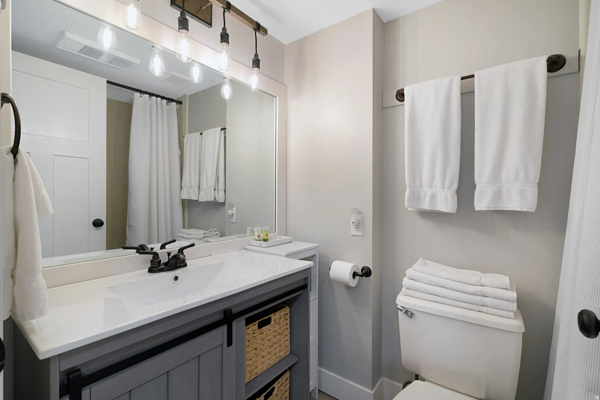 Bathroom featuring a grey vanity with a white countertop, a rectangular sink with a dark bronze faucet, and a large mirror with industrial-style lighting
