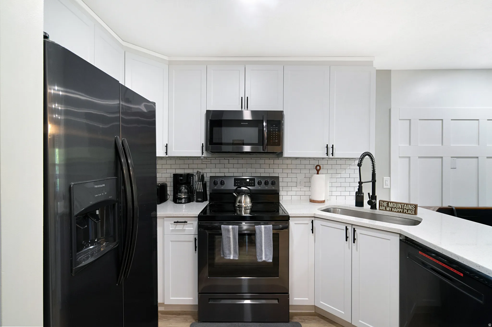 Contemporary kitchen featuring white cabinetry, black hardware, black appliance suite, subway tile backsplash, and light-toned countertops