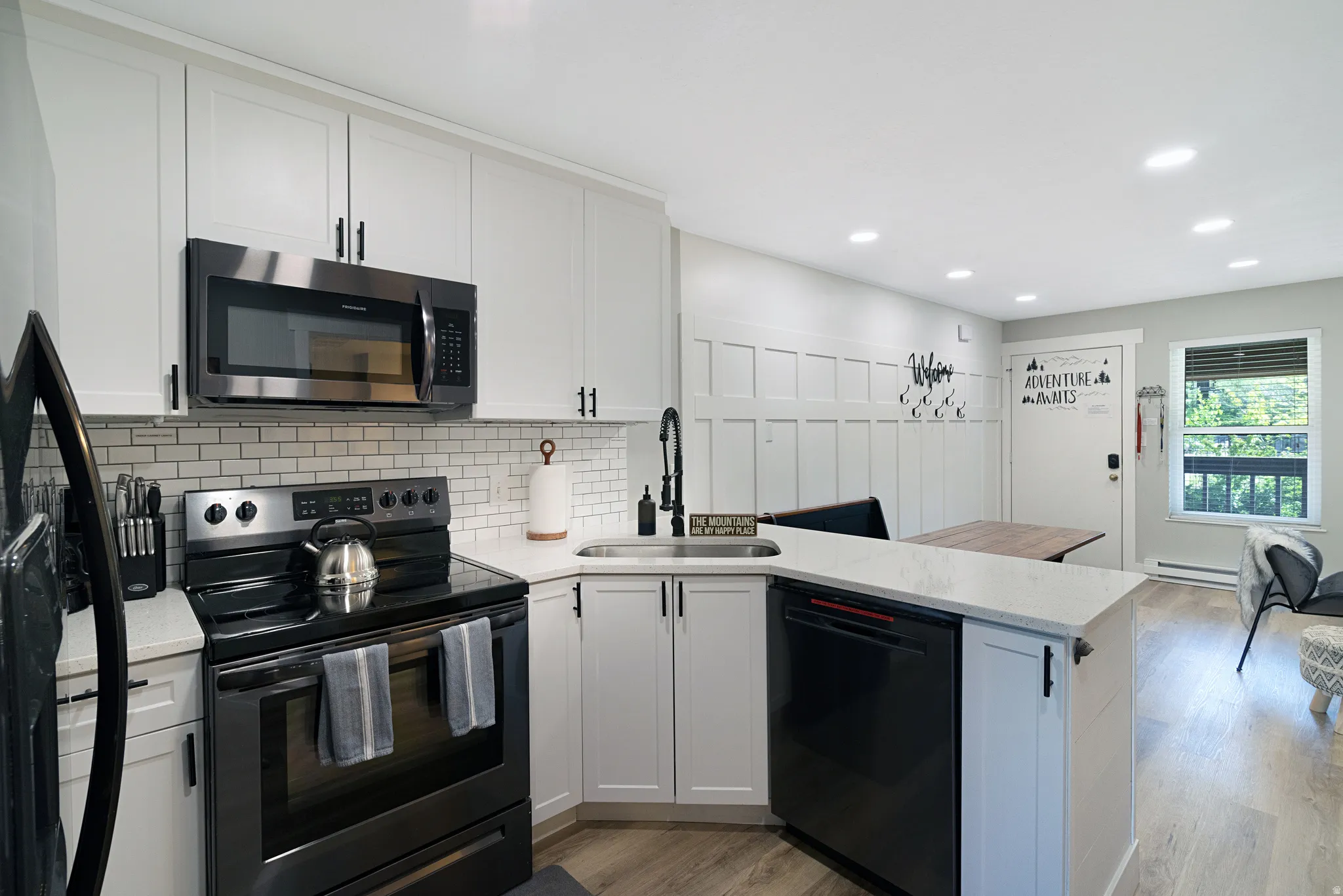 Modern kitchen featuring white shaker cabinetry, stainless steel appliances, a subway tile backsplash, and light wood-finish flooring