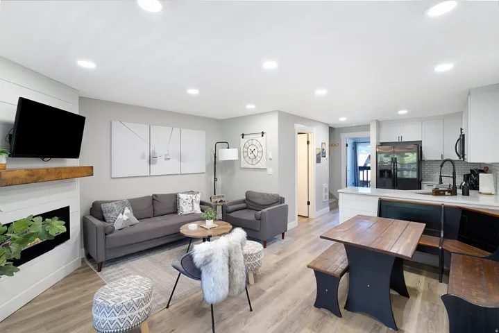 Open-concept living space featuring wood-finish flooring, recessed lighting, and a modern fireplace with a wood mantle