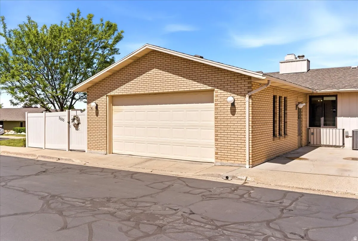 Brick exterior featuring an attached garage with a panel door, vinyl fencing, and a concrete patio