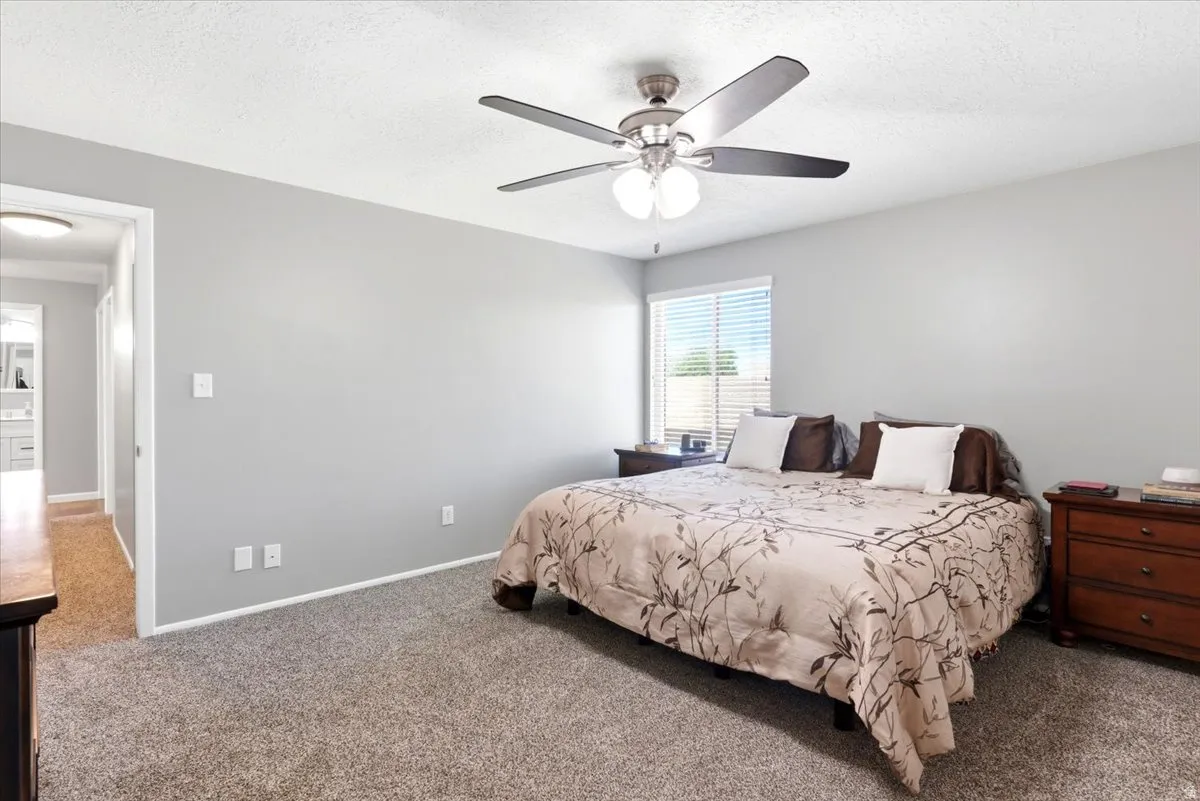 Bedroom featuring neutral gray wall paint, textured carpet flooring, and a ceiling fan with integrated lighting