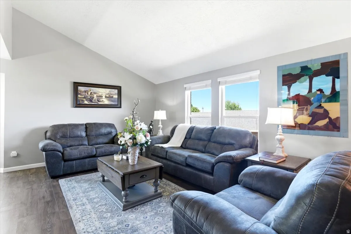 Vaulted ceiling living area featuring wood-finish flooring, light grey wall tones, and multiple windows