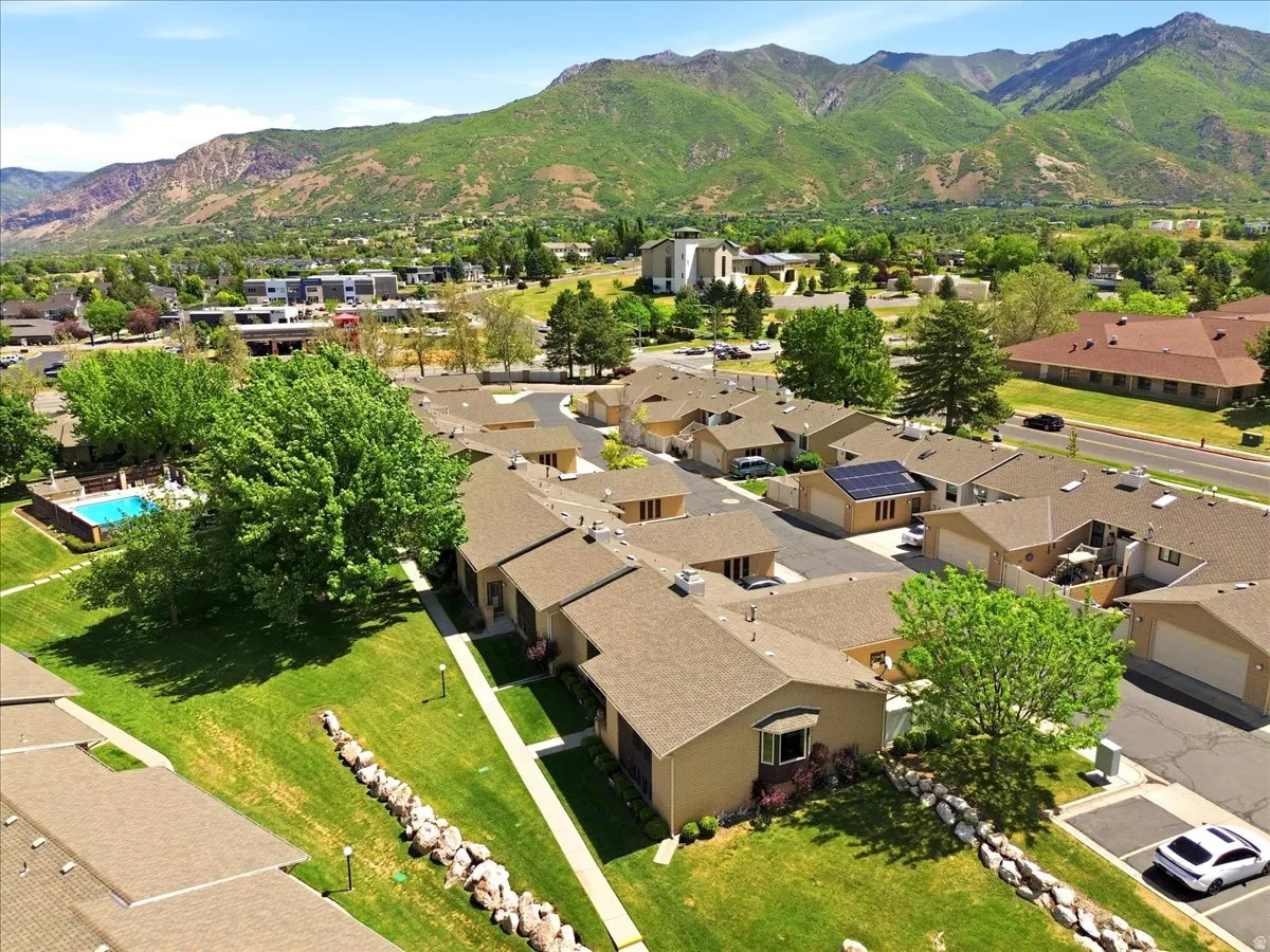 Residential community with mountain backdrop, featuring a swimming pool, mature landscaping, and individual garages