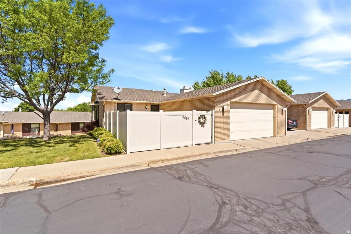 Brick exterior residential building with an attached garage, white privacy fence, and manicured landscaping