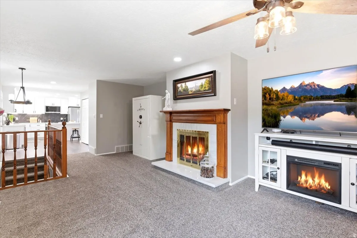 Living area featuring a traditional wood-mantel fireplace with a tiled surround, grey carpeting, and a ceiling fan with light fixture