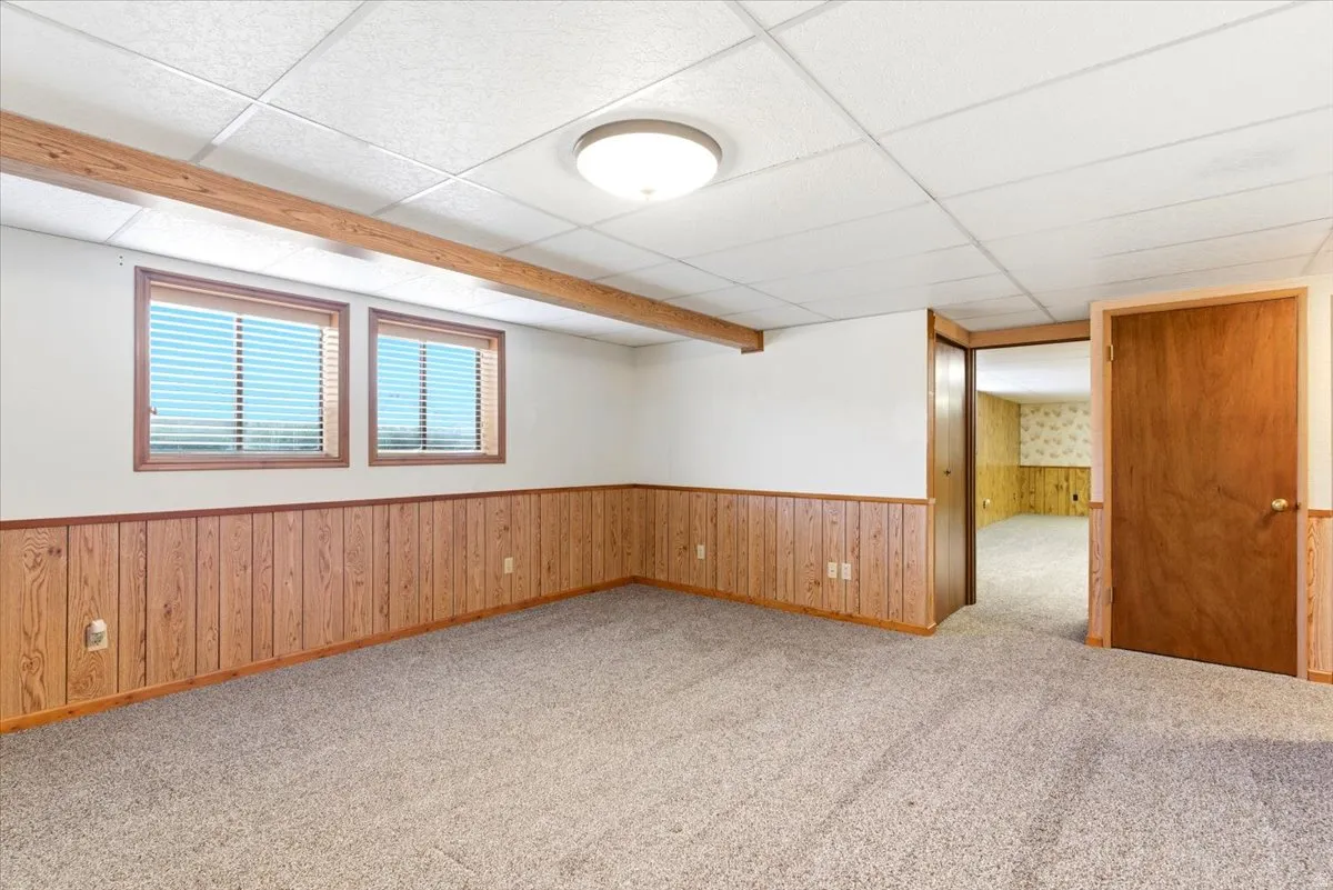 Spacious room featuring light wood-panel wainscoting, two windows with blinds, and neutral carpeting