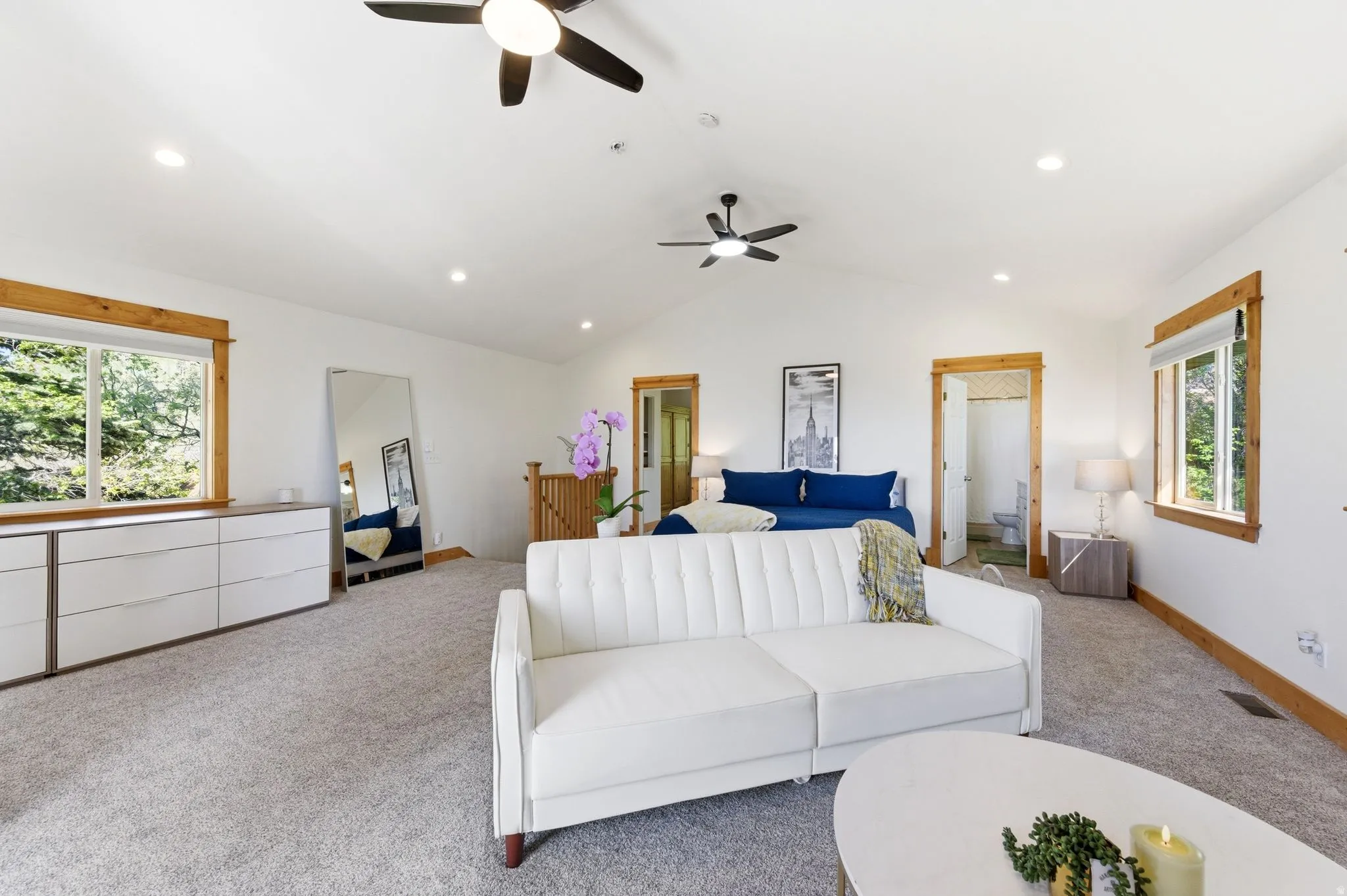 Spacious room featuring vaulted ceilings with two ceiling fans and recessed lighting, light-colored carpet flooring, and natural wood window and door trim