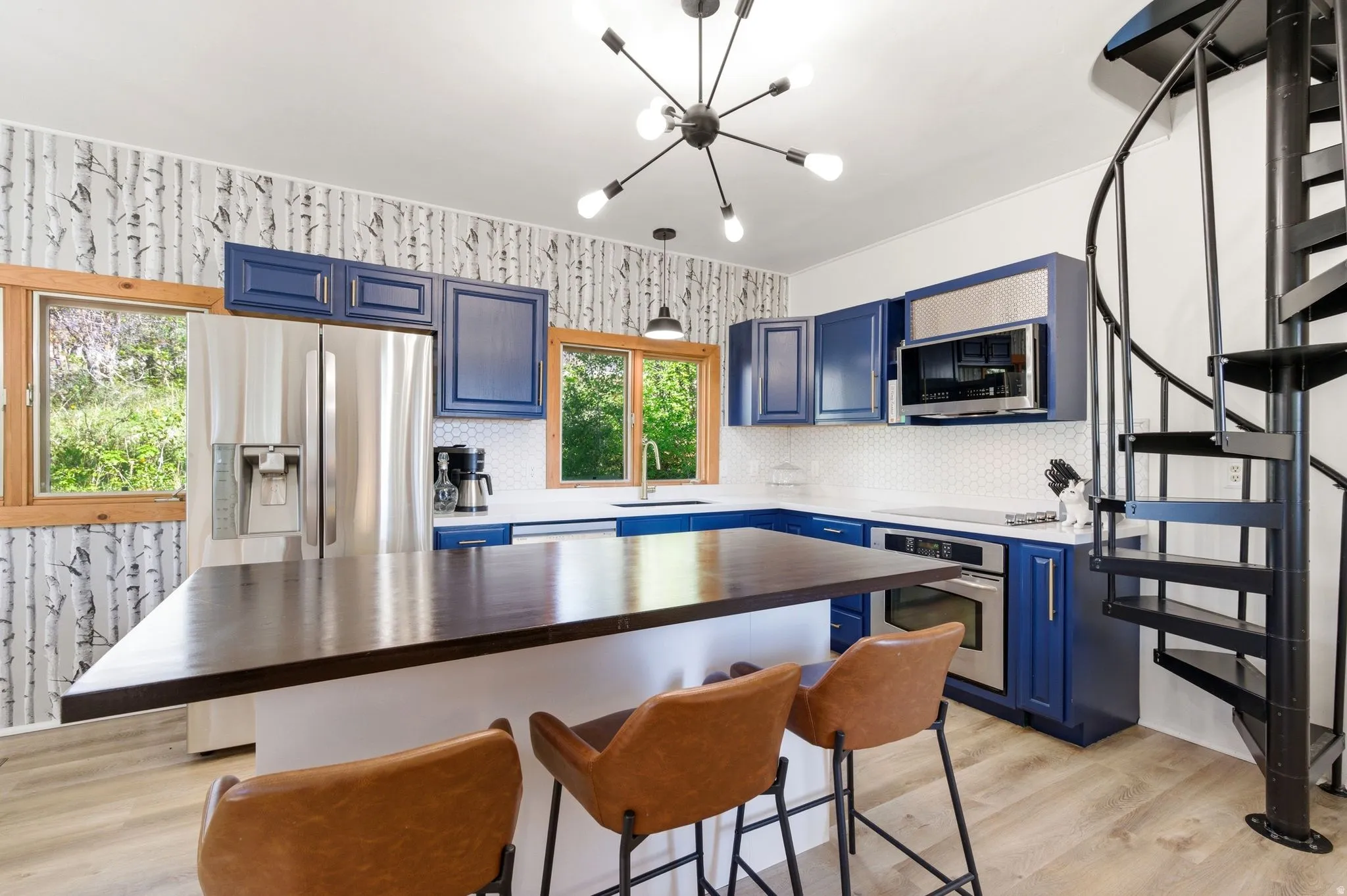 Modern kitchen with blue cabinetry, stainless steel appliances, a spacious island with a dark wood-finish countertop, and a white hexagonal tile backsplash