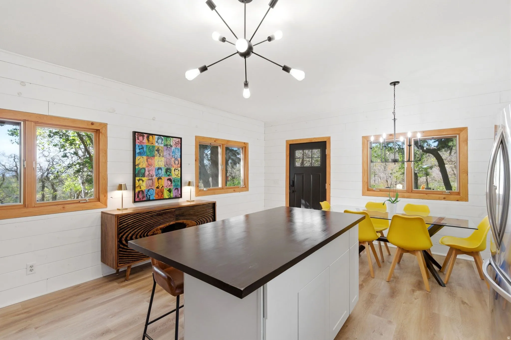 Open-concept living space featuring a central island with a dark countertop, light wood-finish flooring, and white shiplap walls