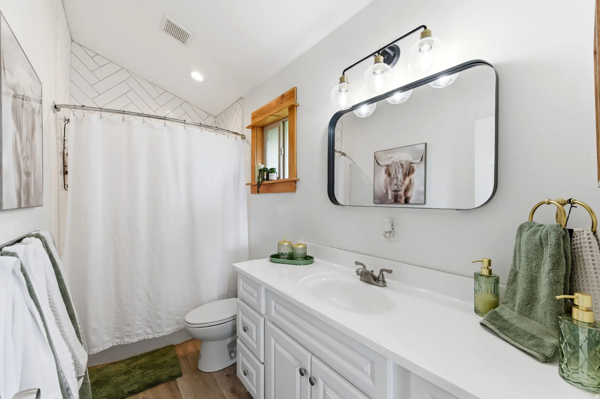 Bathroom featuring a rectangular vanity mirror with a four-light fixture, a white shaker-style vanity with a single sink, and wood-finish flooring