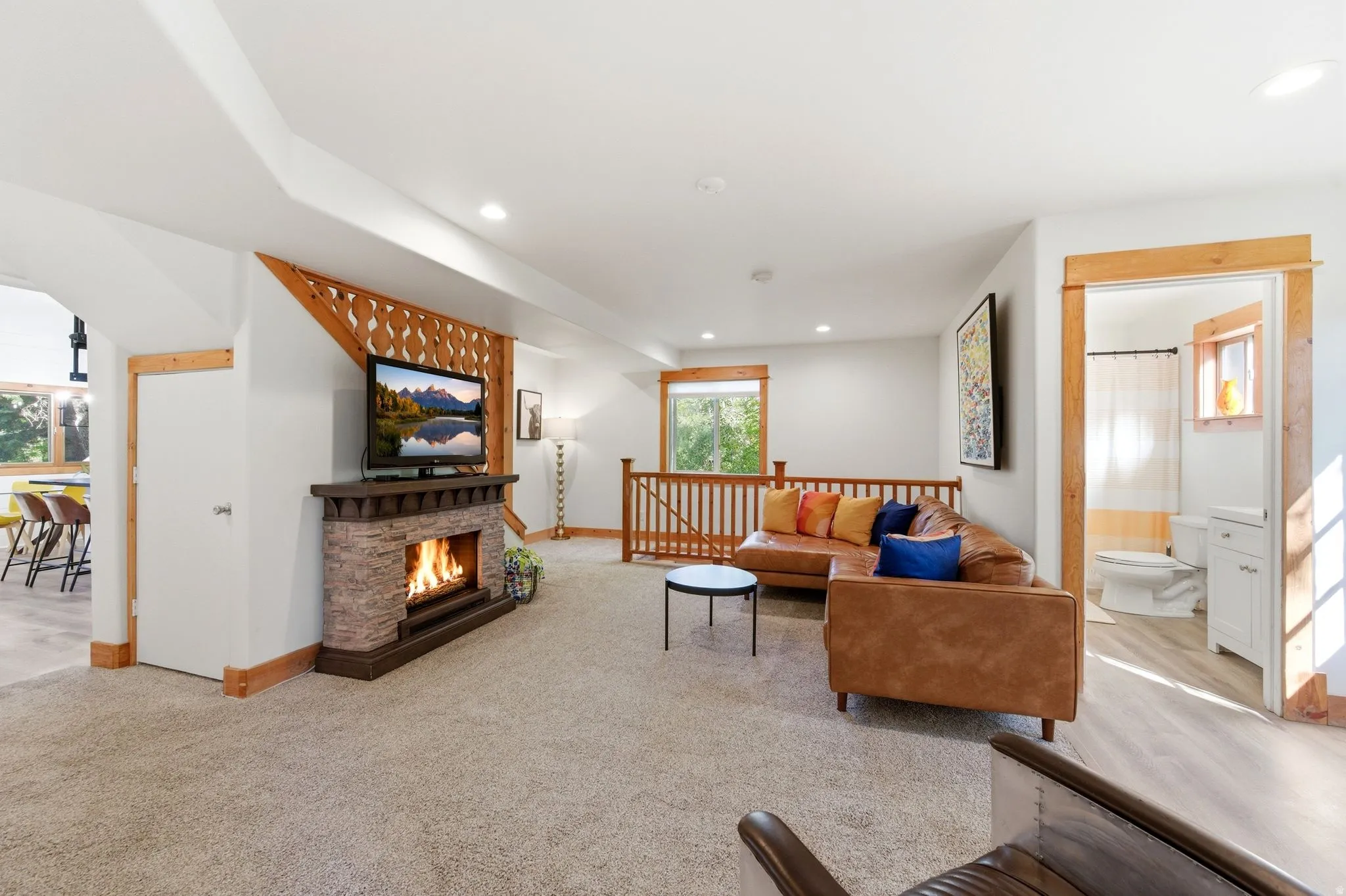 Carpeted living area featuring a stone-clad fireplace with a dark wood mantel, recessed lighting, wood-finish flooring, and natural wood trim accents