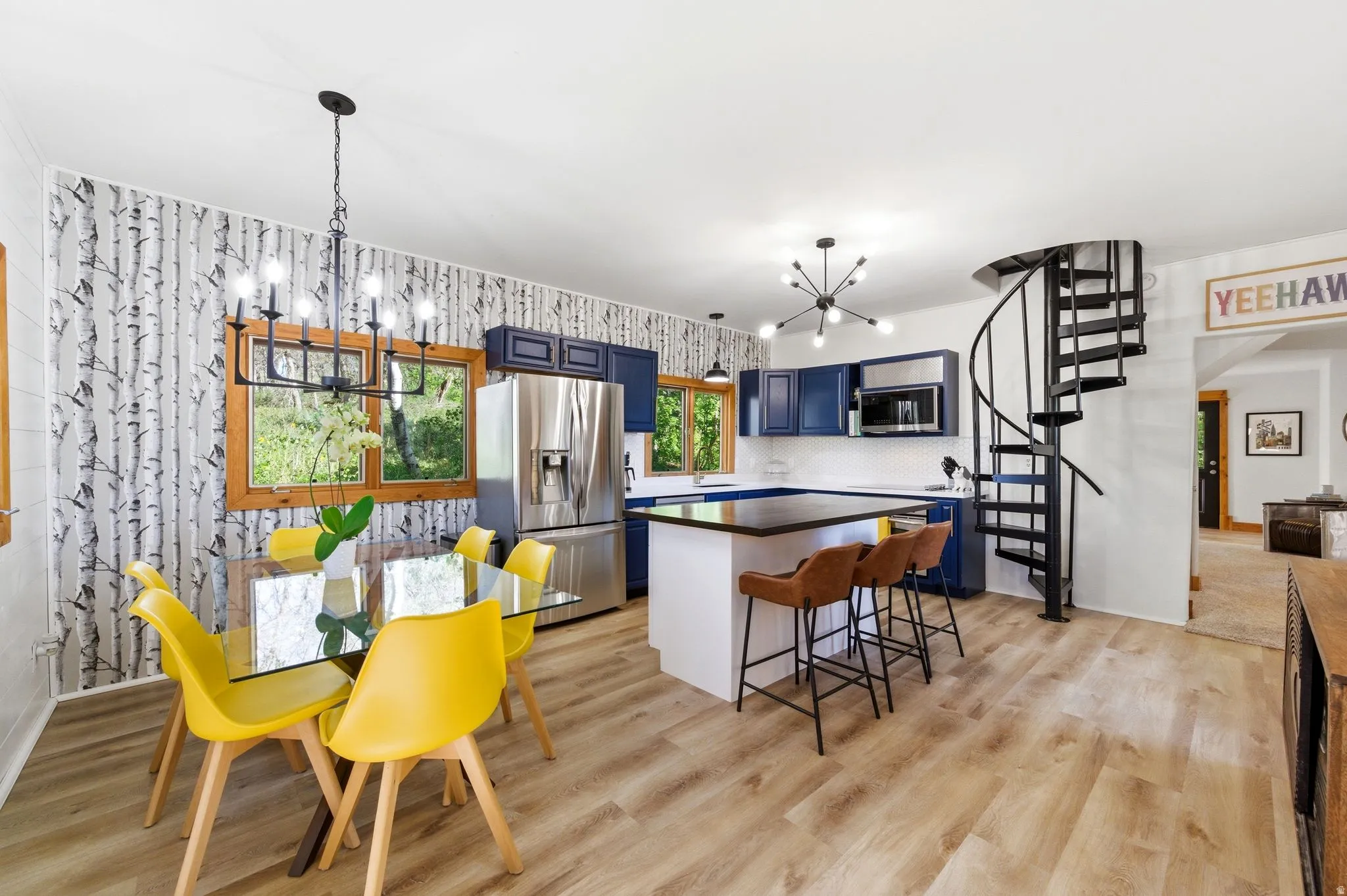Open-concept living space with wood-finish flooring, a spiral staircase, and a kitchen featuring stainless steel appliances, blue cabinetry, and a black countertop island