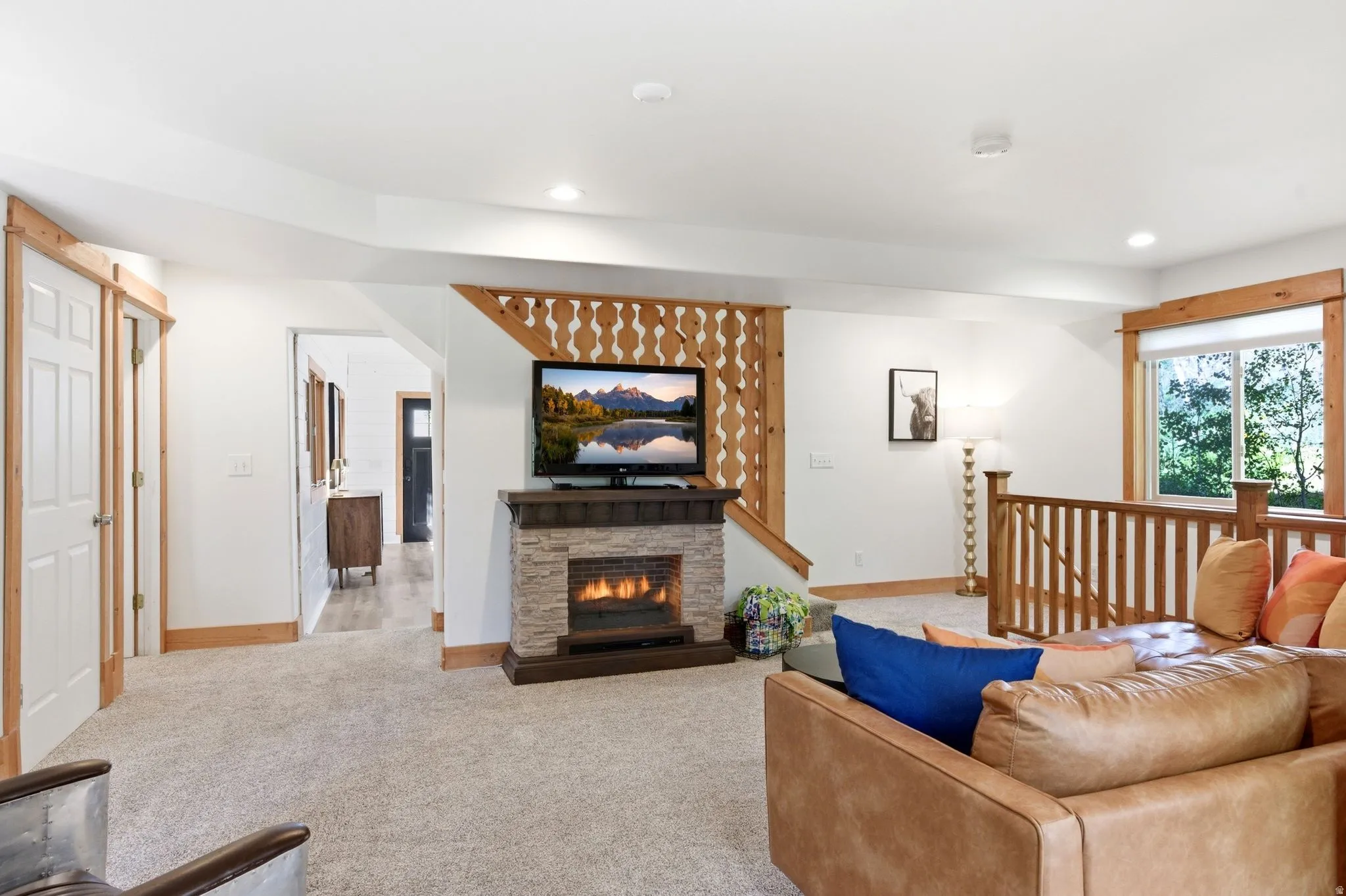 Living area featuring a stone-clad fireplace, recessed lighting, carpet flooring, a large window, and wooden staircase railing