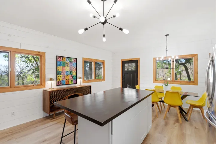 Open-concept living space featuring a central island with a dark countertop, light wood-finish flooring, and white shiplap walls