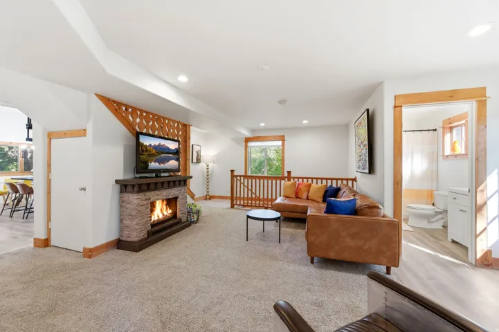 Carpeted living area featuring a stone-clad fireplace with a dark wood mantel, recessed lighting, wood-finish flooring, and natural wood trim accents