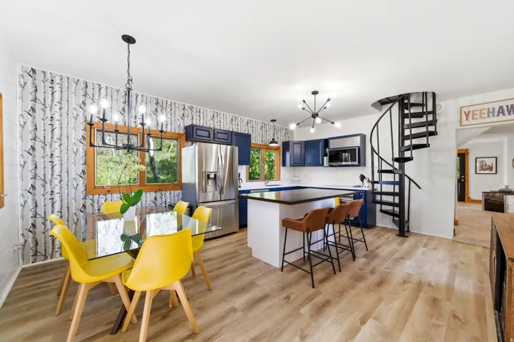 Open-concept living space with wood-finish flooring, a spiral staircase, and a kitchen featuring stainless steel appliances, blue cabinetry, and a black countertop island
