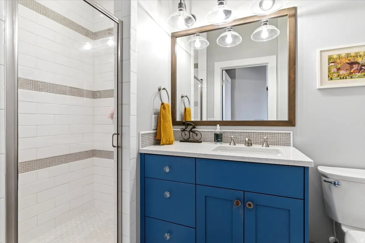 Bathroom featuring a glass-enclosed shower with white subway tile and decorative accent bands, a blue vanity with a white countertop and integrated sink, a framed mirror, and a wall-mounted light fixture