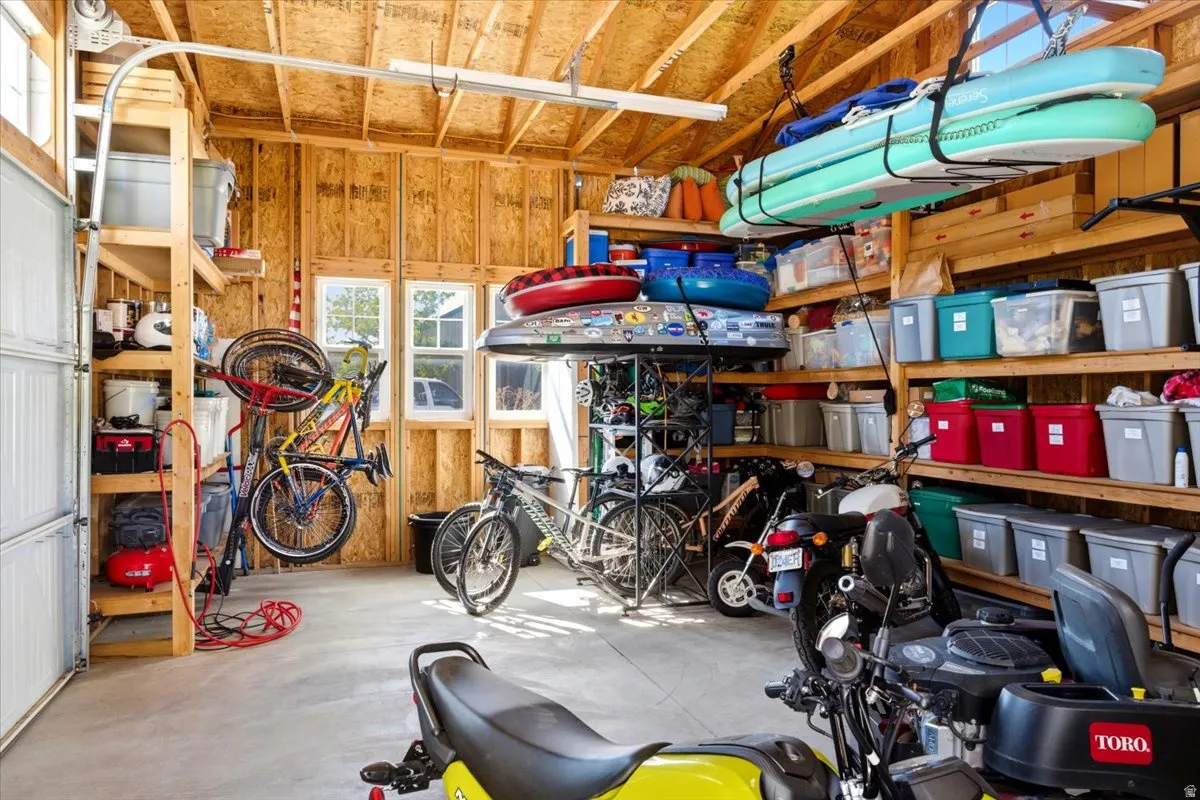 Spacious garage featuring exposed wood framing, concrete flooring, multiple windows, and a roll-up garage door