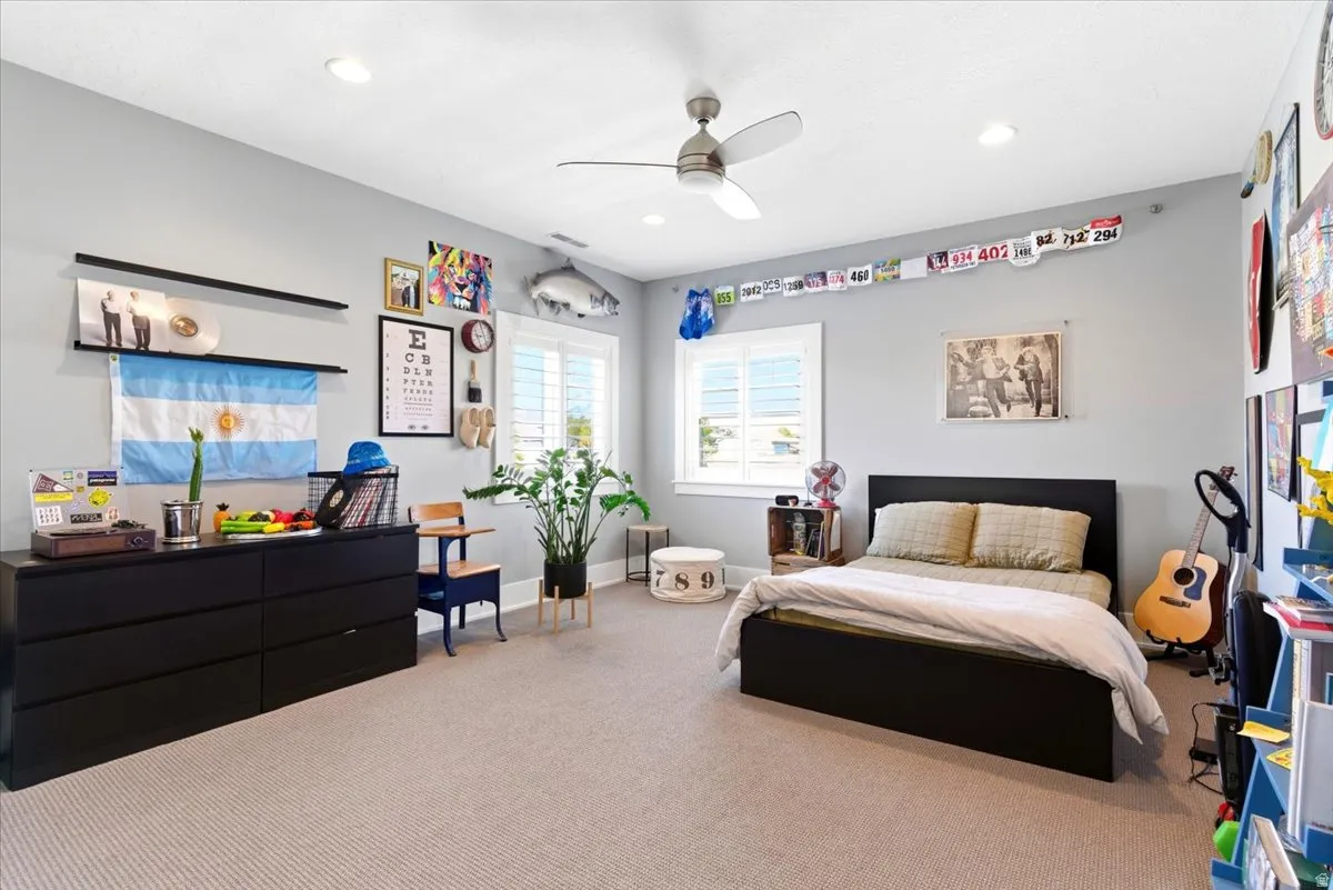 Spacious room featuring light gray walls, recessed lighting, a ceiling fan, plush carpet flooring, and two windows with white louvered shutters