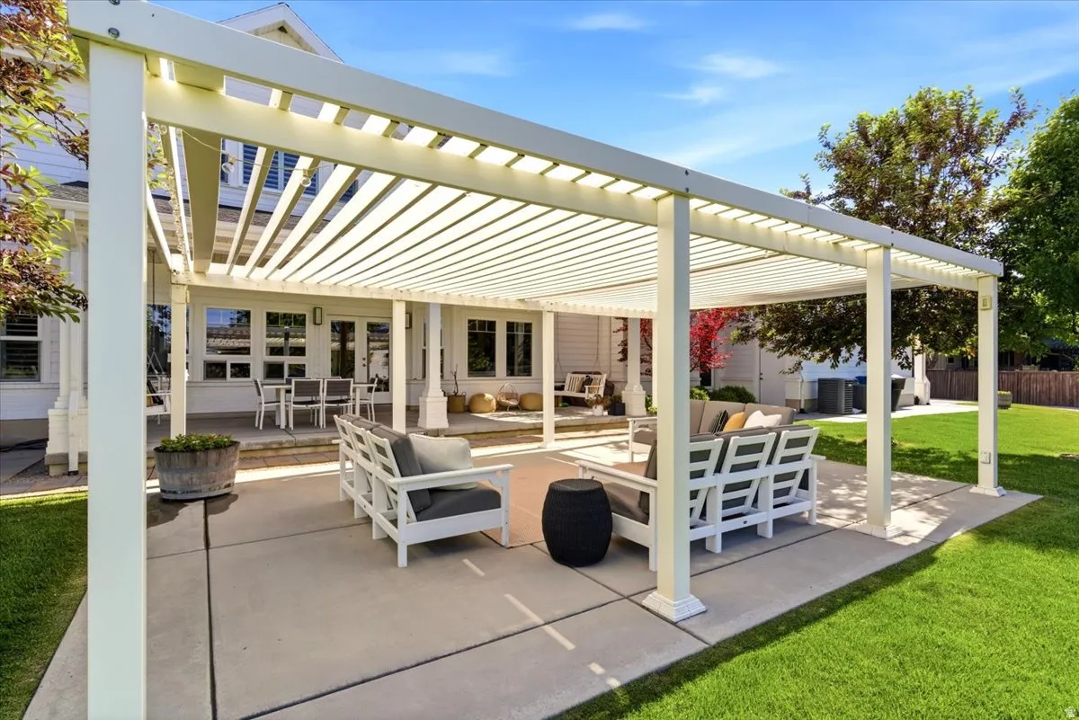Expansive patio featuring a louvered pergola, concrete surfacing, and direct access to the interior via multiple doors