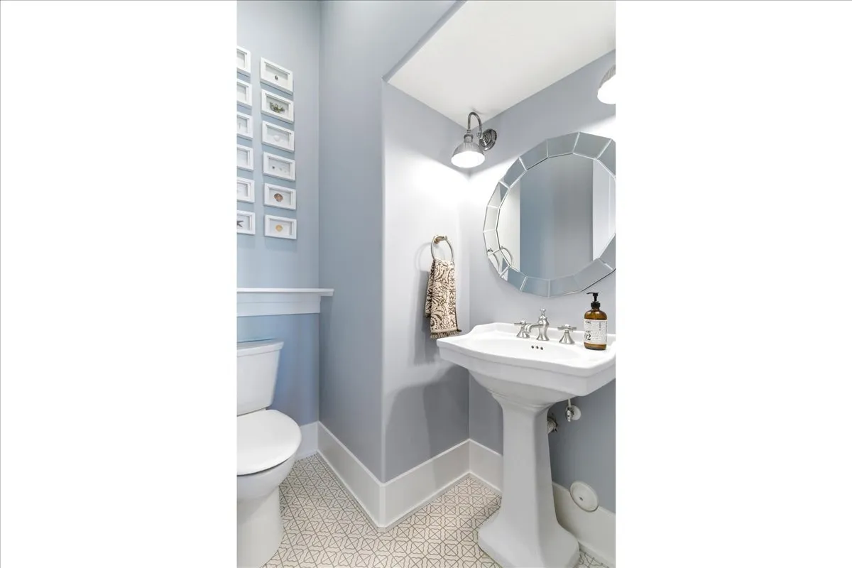 Pedestal sink with polished chrome fixtures, accented by a decorative round mirror