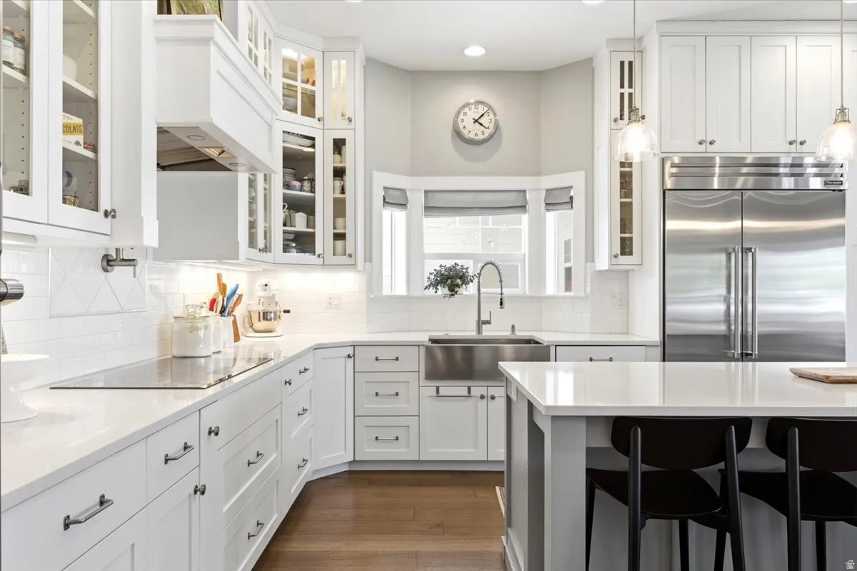 Contemporary kitchen featuring white cabinetry, a large stainless steel refrigerator, stainless steel farmhouse sink, white countertops, and wood-finish flooring