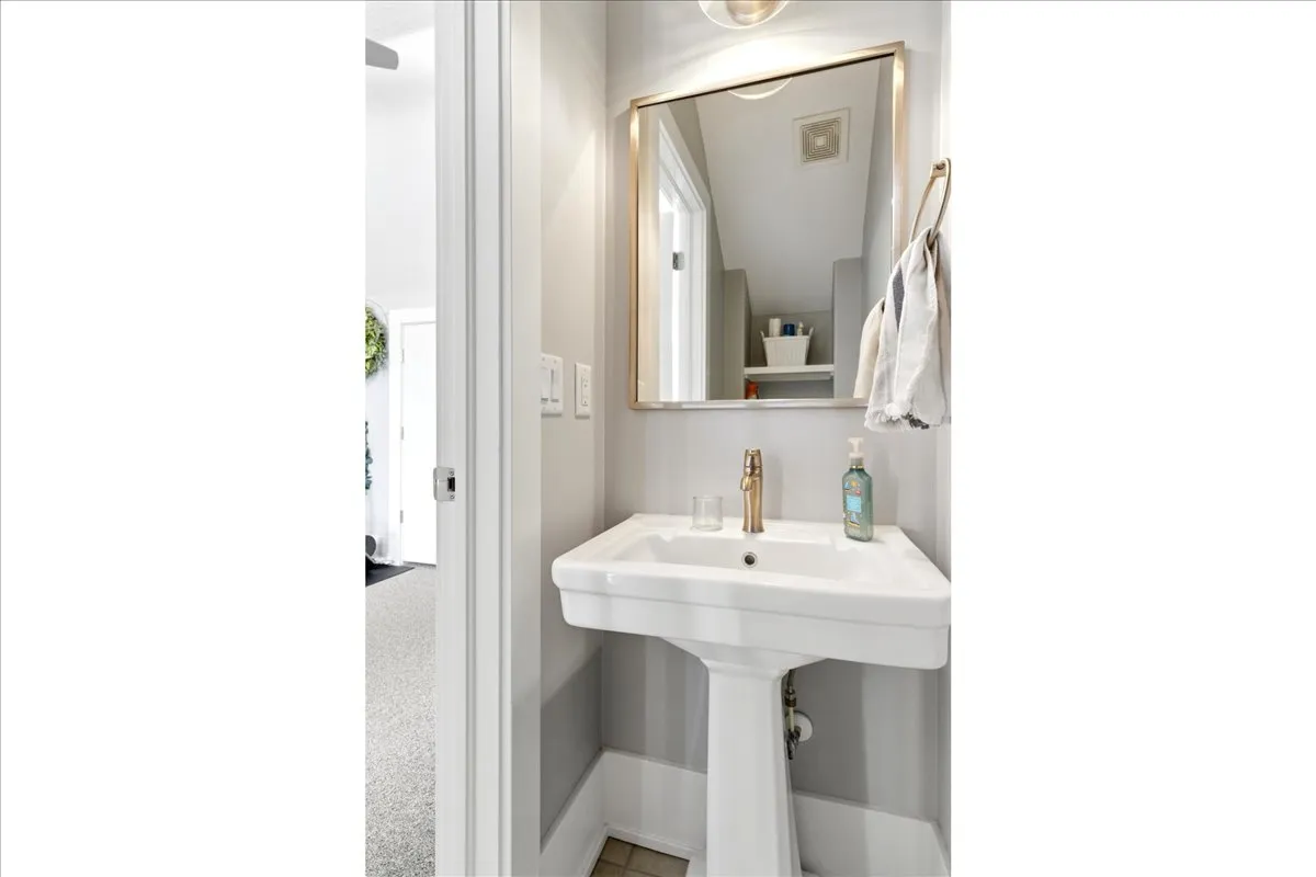 White pedestal sink with a gold-tone faucet, framed mirror, and light gray wall paint