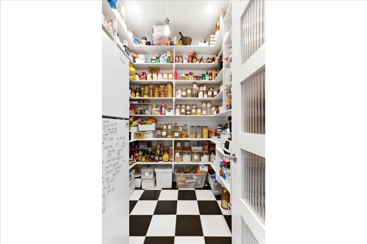 Pantry featuring extensive built-in shelving, checkered flooring, white French doors with reeded glass panels, and a full-size refrigerator