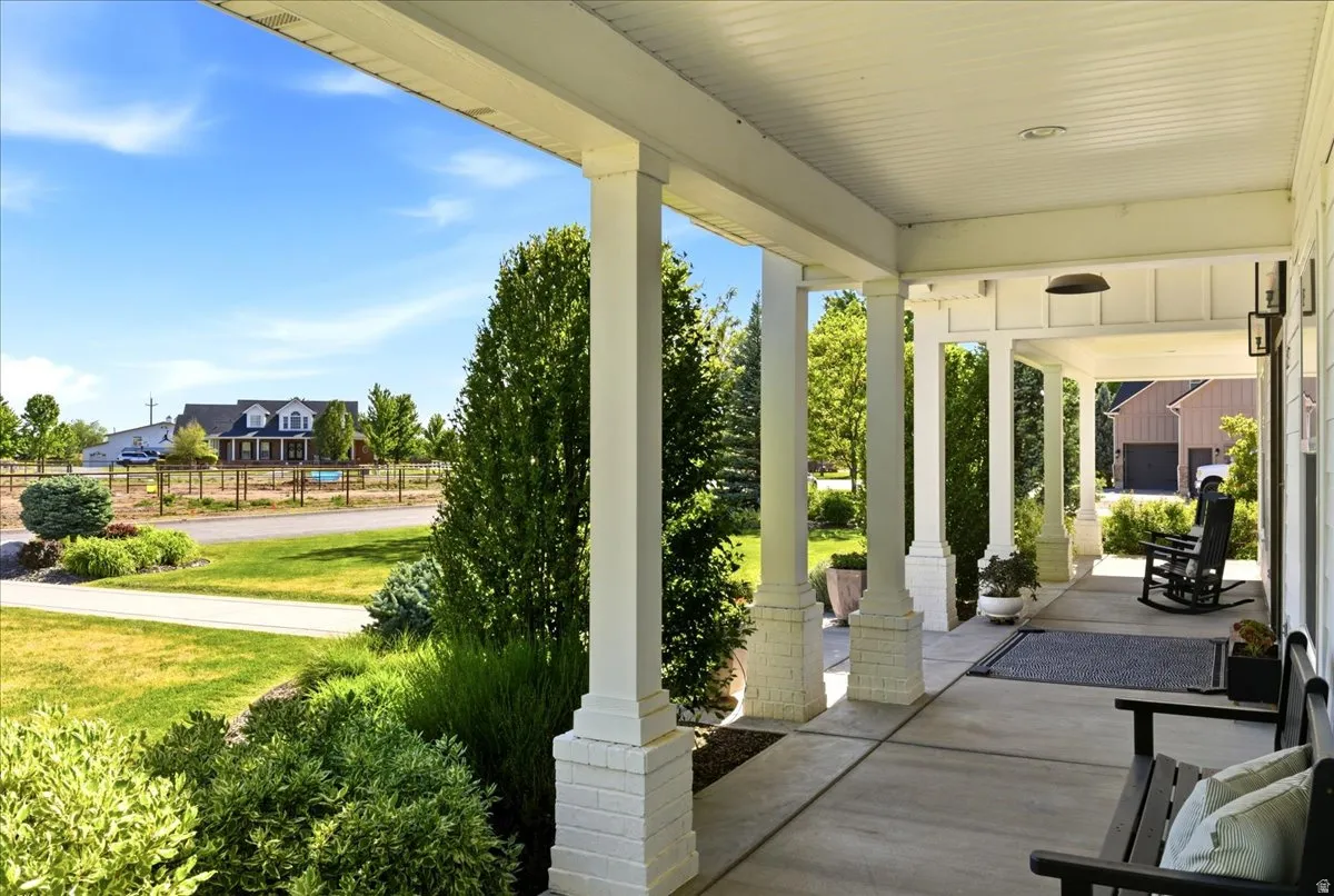 Expansive covered front porch featuring white columns with brick bases, planked ceiling, and a concrete surface