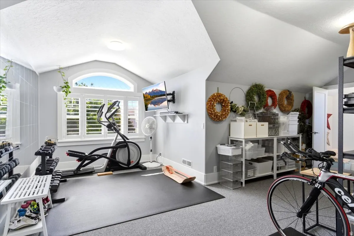 Vaulted ceiling featuring a large arched window with plantation shutters, light gray wall paneling, and a mounted flat-screen display