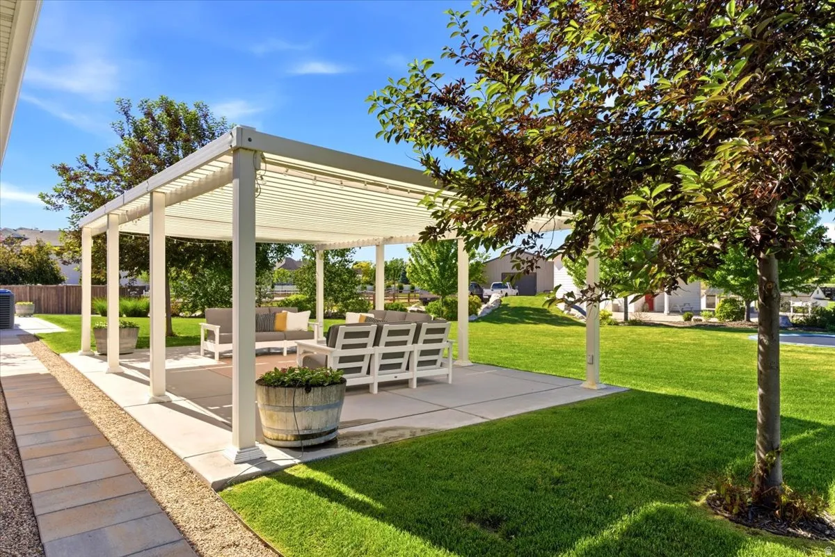 Backyard patio featuring a white pergola, concrete slab, and an expansive lawn