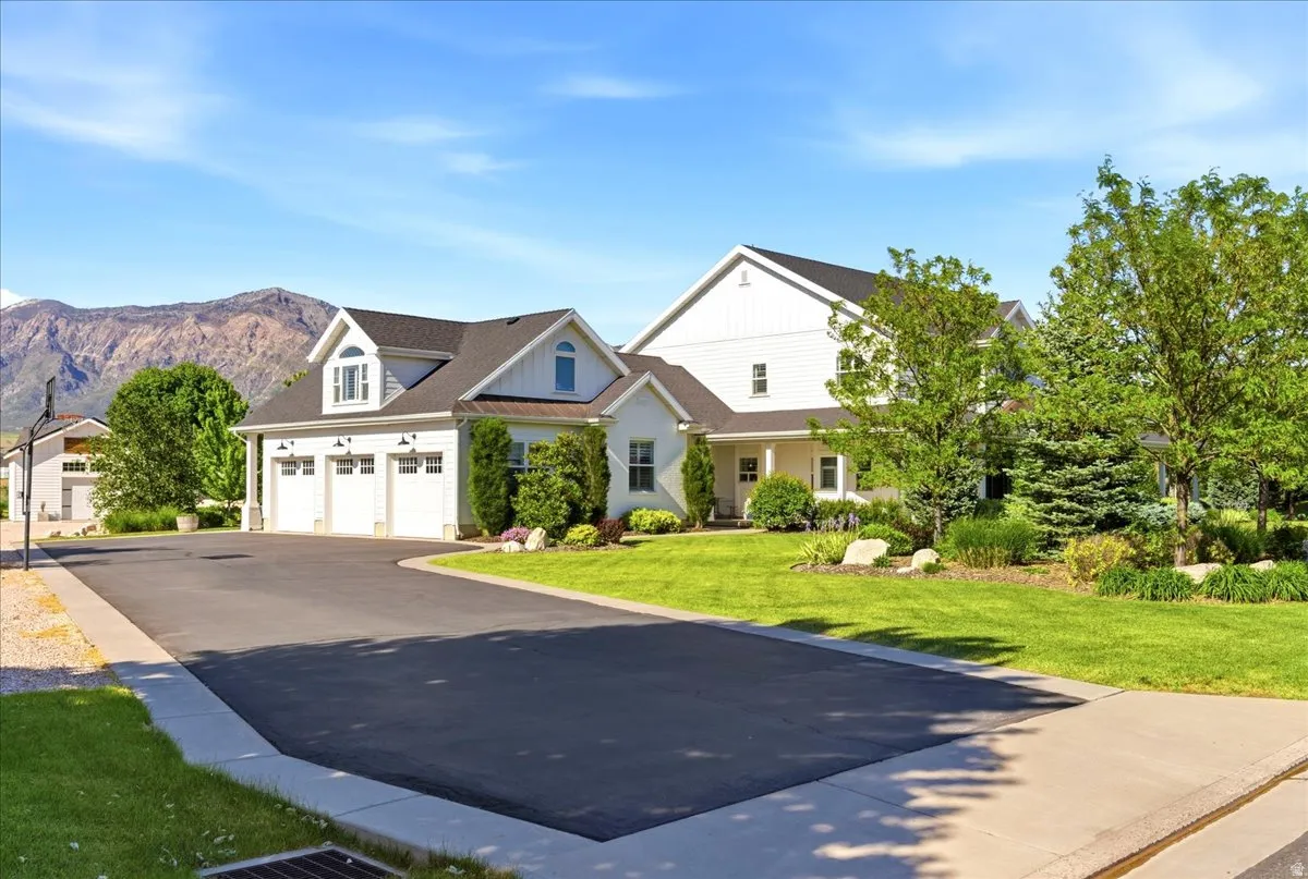 White multi-level residence featuring a three-car garage, dark shingled roof, and a mountain backdrop