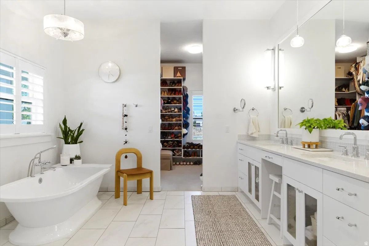 White bathroom featuring a freestanding soaking tub with chrome fixtures, a double vanity with stone countertops and undermount sinks, and a large mirror