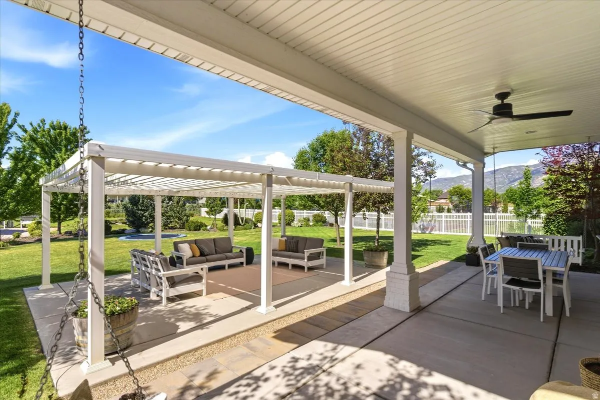 Expansive concrete patio featuring a covered portion with a ceiling fan and a separate pergola-covered section