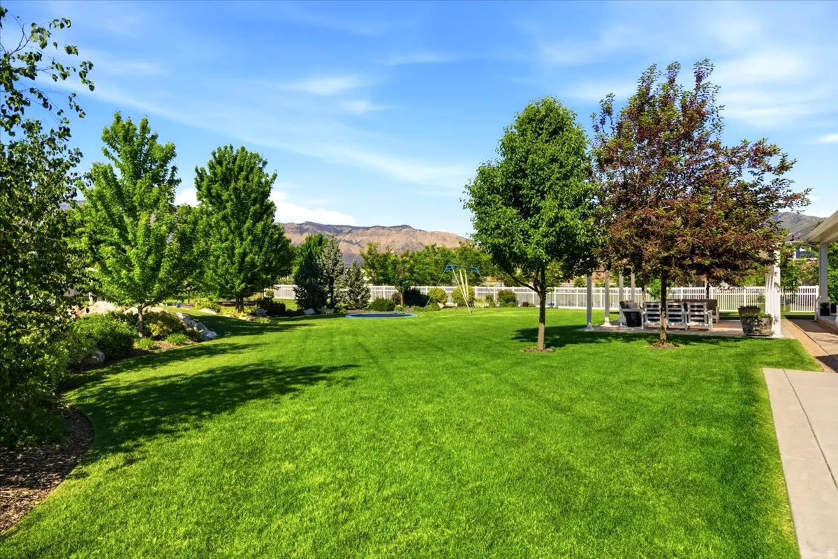 Expansive grassy yard featuring mature trees and a white picket fence