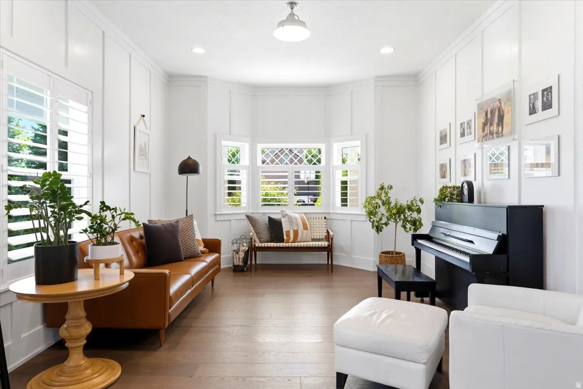 Living space with wood-finish flooring, white paneled walls, recessed lighting, and a multi-pane bay window featuring white plantation shutters