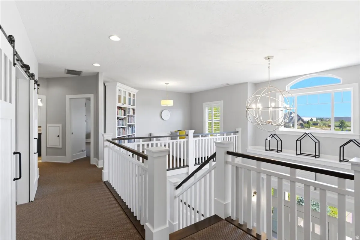 Upper-level landing featuring a white balustrade with dark wood-finish handrails, a large arched window, a spherical chandelier, recessed lighting, and a built-in bookcase