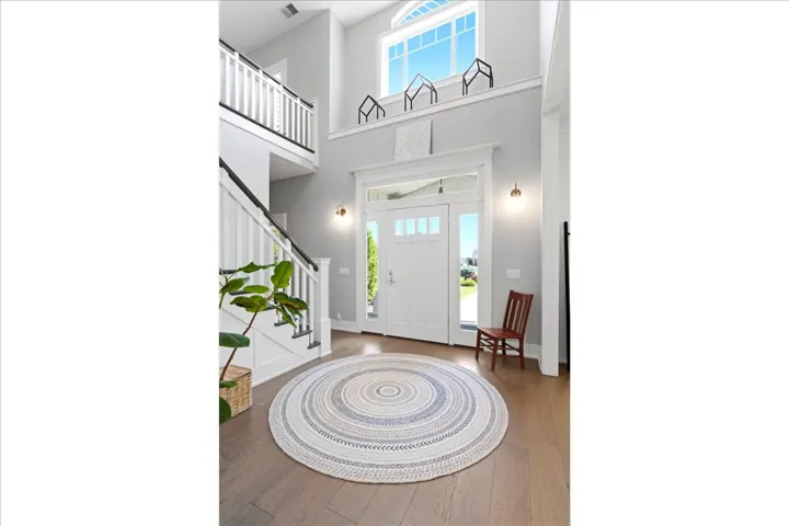 Two-story foyer featuring a prominent white staircase with dark handrails, wood-finish flooring, a transom window above the entry door, and a second-story window providing ample natural light